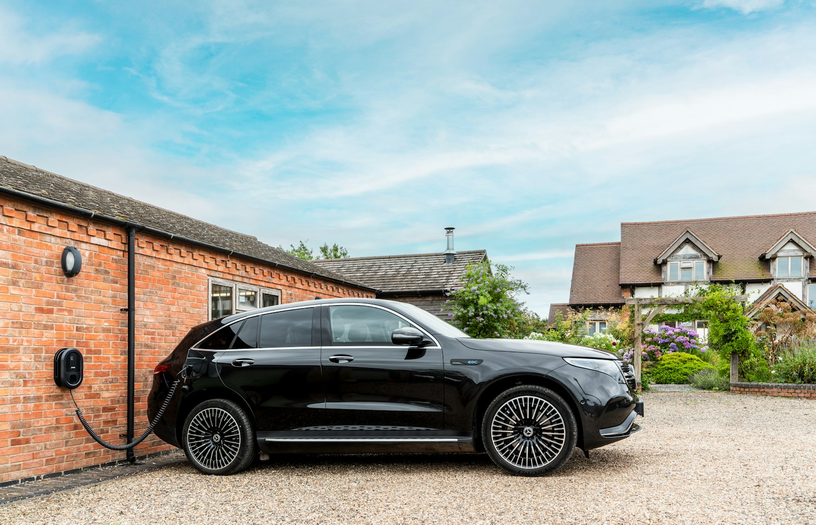 Electric car charging from a wall-mounted charger beside a brick home in the UK